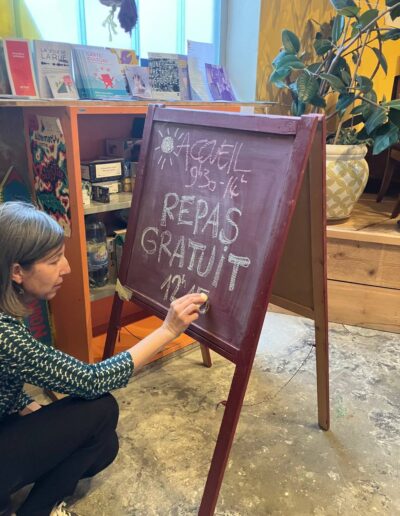 Une bénévole écrit à la craie "Repas gratuit" sur un tableau noir.