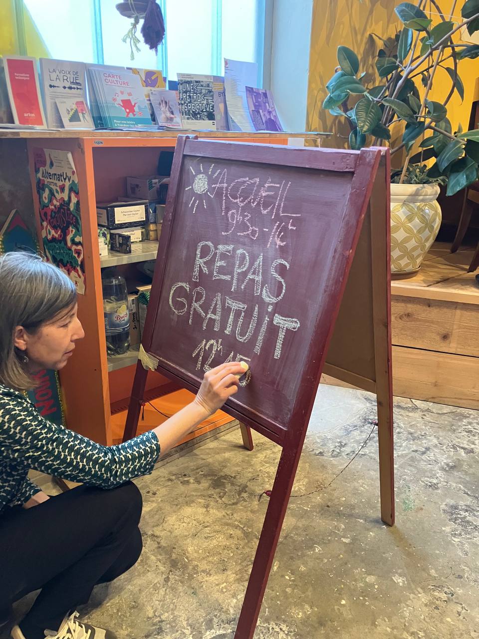 Repas gratuit ESCAPE Une bénévole écrit à la craie "Repas gratuit" sur un tableau noir.